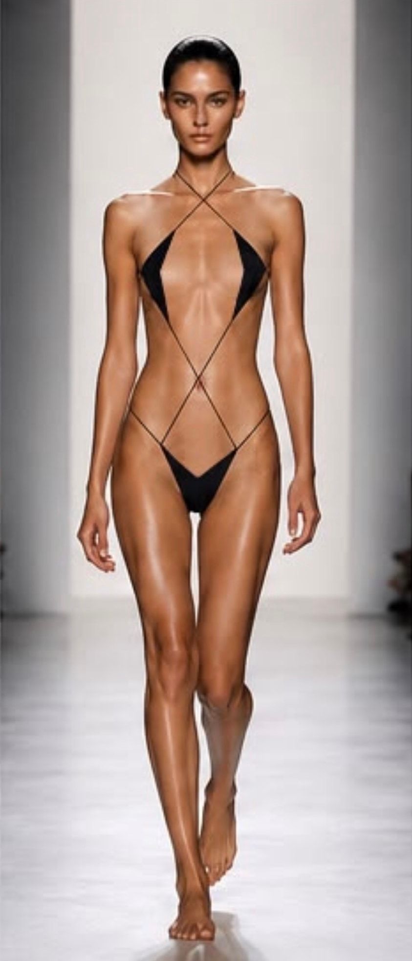 A model on the runway in CHIASTI, fine black cords crossing at the neck and waist.
